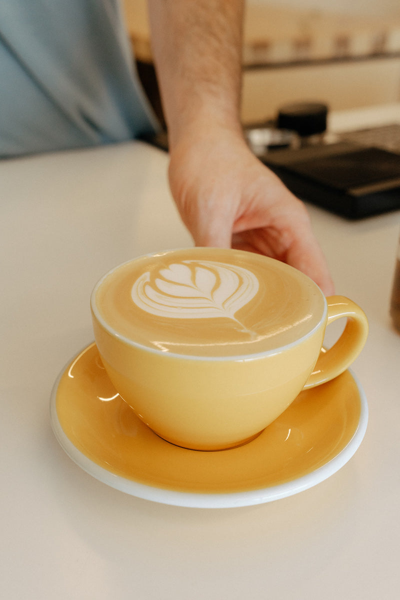 Barista setting down a latte in a yellow cup