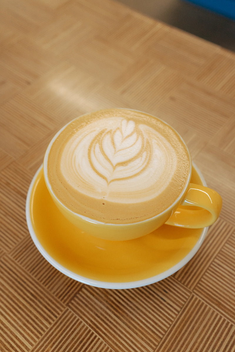 Latte with leaf latte art in a yellow cup and saucer
