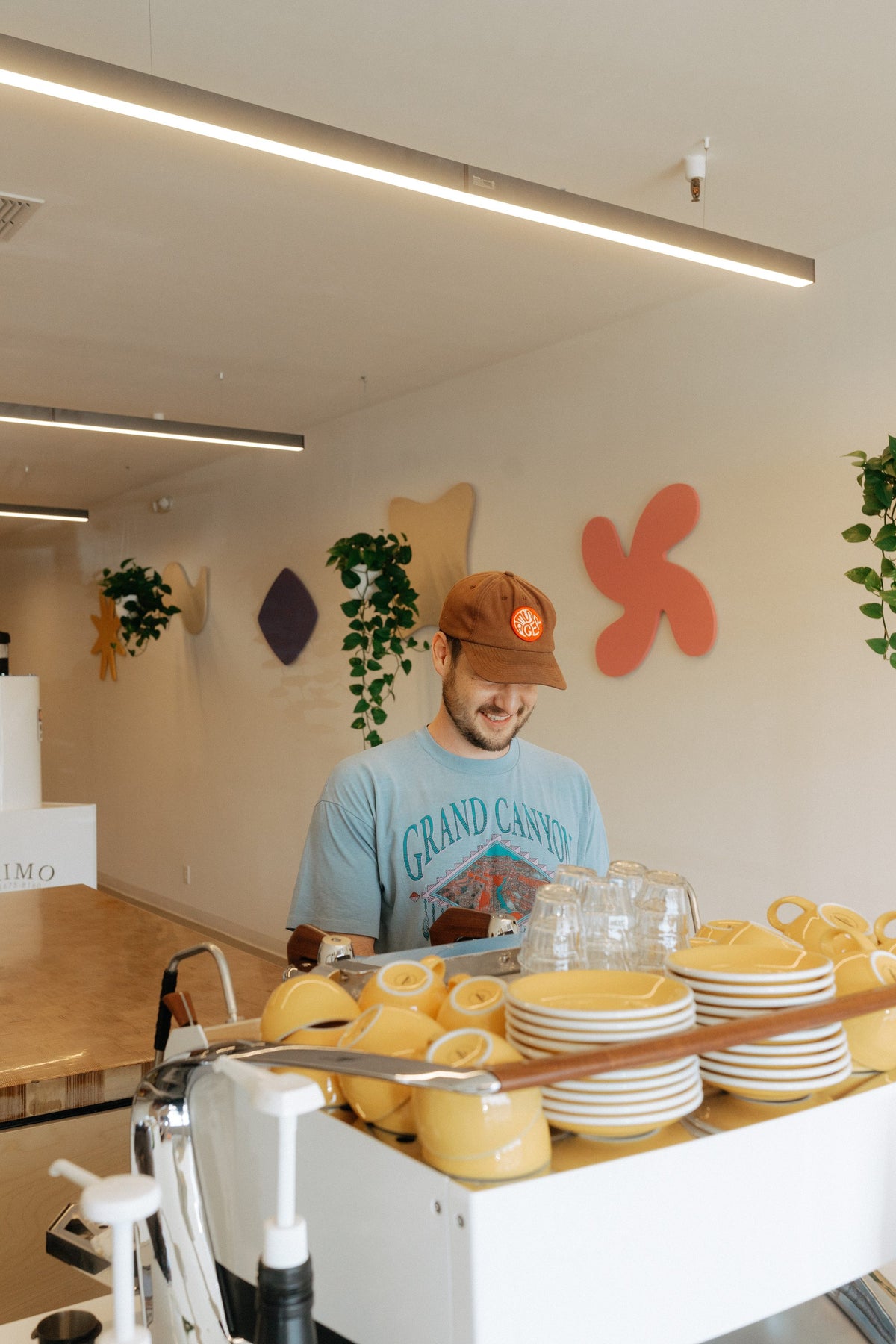 Smiling WeBe barista behind the counter under the WeBe icon wall