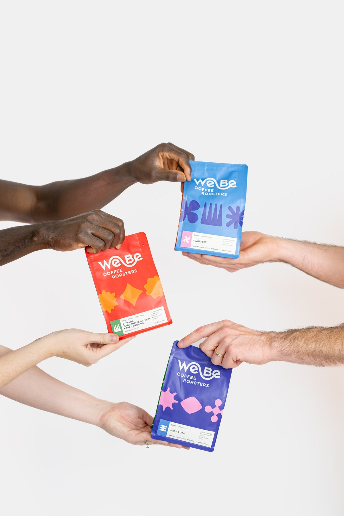 Hands passing colorful bags of WeBe coffee