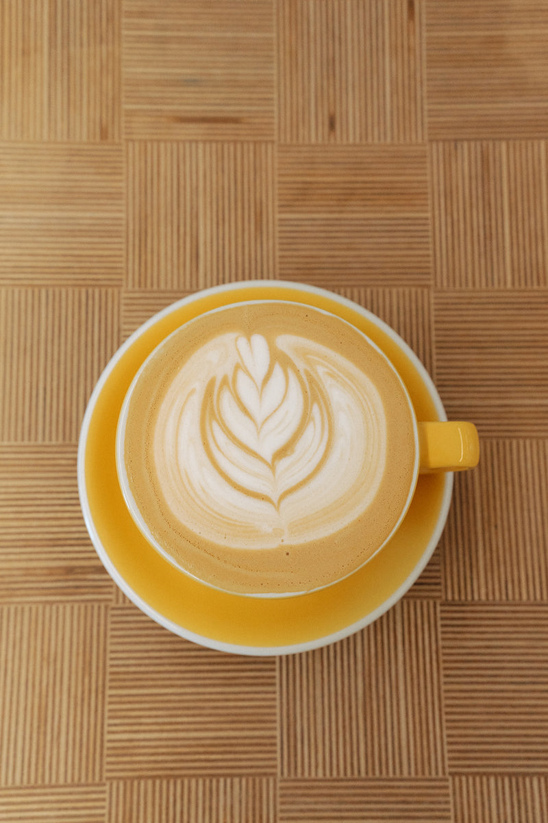 Latte art in a yellow cup on a wood table, seen from above