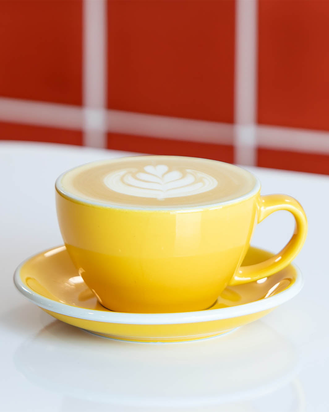 Yellow cup of cappuccino with latte art on a white surface with red tile background